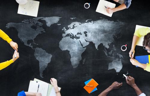 Map of the global surrounded by various people's hands holding or writing in notebooks